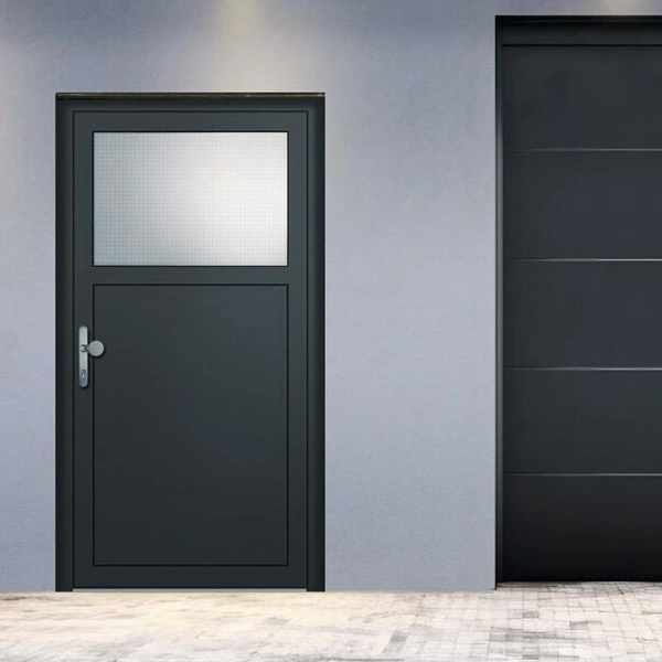 Front entry door in dark gray with a frosted rectangular window above, set in a light-gray exterior wall next to a tall black garage door.